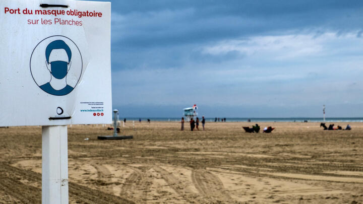 People enjoy the beach next a sign, which reads as "Face masks must be worn on Les Planches" in Deauville, Northwestern France, on August 2, 2021.